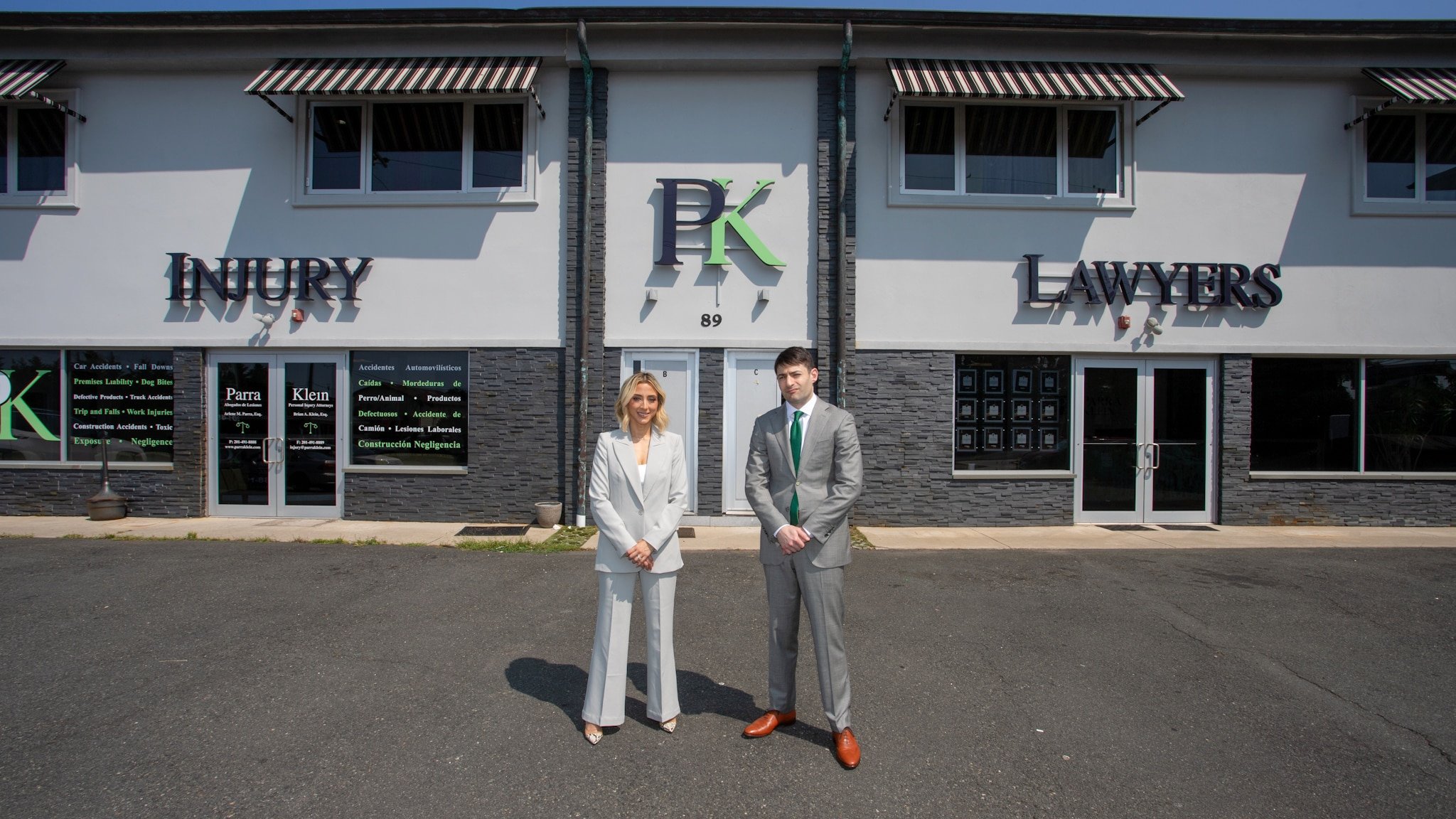 Arlene M. Parra and Brian A. Klein standing outside the Parra Klein office at 89 US-46 in Elmwood Park, under the Injury Lawyers sign